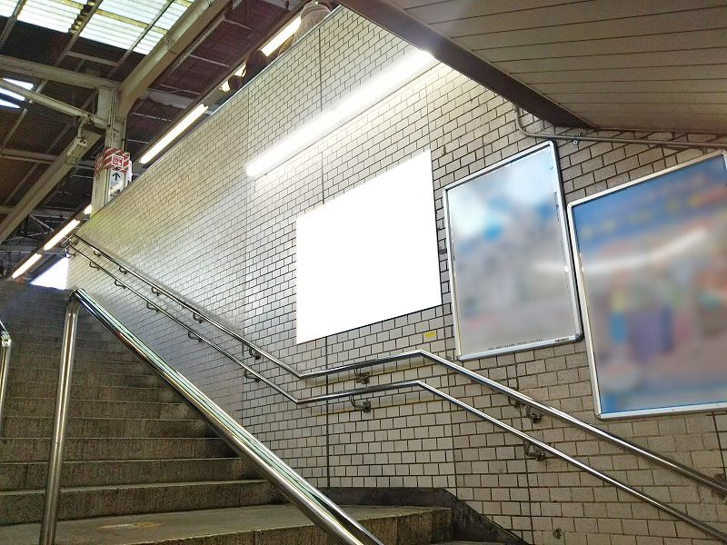 池袋駅集中貼りの掲載写真です。この写真はホーム階段の横壁面にB0サイズのポスターを貼り出しています。